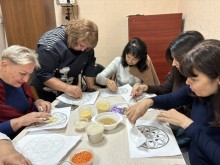 Група освітян Добропільської громади під час мандала-терапії творчо працюють за великим столом, де розкладено кольорові крупи, аркуші та зразки мандал.