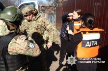 Діти у захисному спорядженні чекають загрузку до автомобіля. Поліцейський поруч.