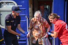 Рятувальник та медик допомагають маломобільній жінці похилого віку вийти з потяга