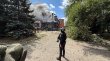 Правоохоронець стоїть біля будівлі, яка горить після ворожого обстрілу