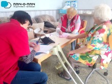 Представниці Червоного хреста проводять медичне обстеження, поруч сидить жінка похилого віку. На столі лежать медикаменти та медичні прилади.