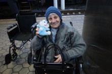 Евакуація літньої жінки, поруч стоїть крісло колісне, жінка тримає дитячу іграшку та посміхається