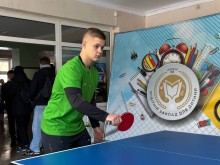 Хлопець у зеленій футболці грає у настільний теніс та тримає ракетку у руках.