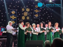 Місцевий колектив народної творчості. Артисти стоять на сцені у зелених костюмах, в руках тримають папки з текстом пісень.