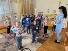 Практикантка педколеджу проводить фізкультурне заняття з дошкільнятами: діти підняли м’ячики вгору, повторюючи рух.