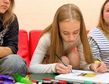 Дівчина з довгим волоссям тримає олівець у руках та щось пише на папері.