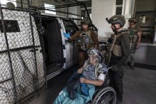 Парамедики запрошують літню жінку до евакуації на спецавтомобілі, який захищено антидроновою сіткою