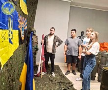 Група молодих людей розглядають військову атрибутику. Поруч стоїть манекен у військовій формі.