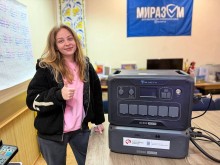 Молода жінка, тримає великий палець угору, поруч на столі стоїть зарядна станція.