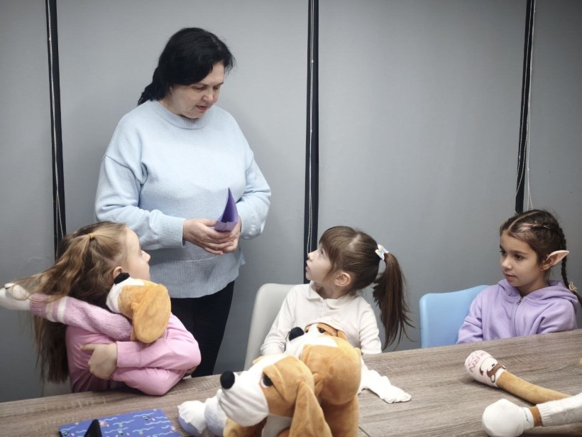 Педагог спілкується з дівчатками, які обіймають своїх песиків Хібукі, отримуючи емоційну підтримку в межах проєкту «Теплі обійми»