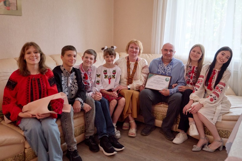 Велика родина Трембачів. Дівчата та хлопці у вишиванках з посмішкою на обличчі. Голова родини тримає в руках ордер на будинок.