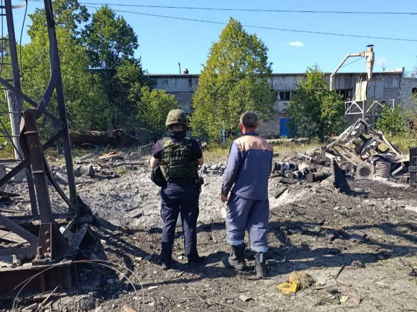 Правоохоронець та працівник підприємства дивляться на зруйновані промислові будівлі