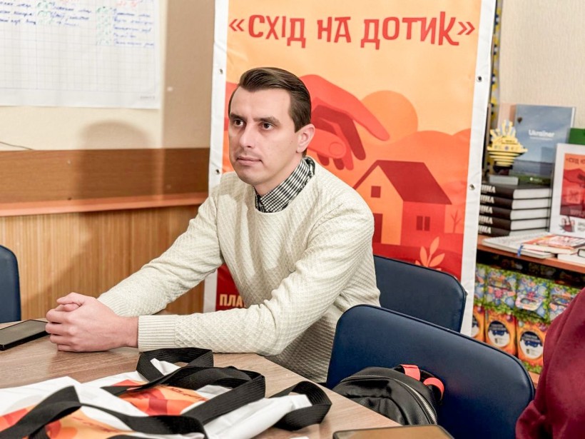 Учасник проєкту, позаду банер з написом "Схід на дотик"