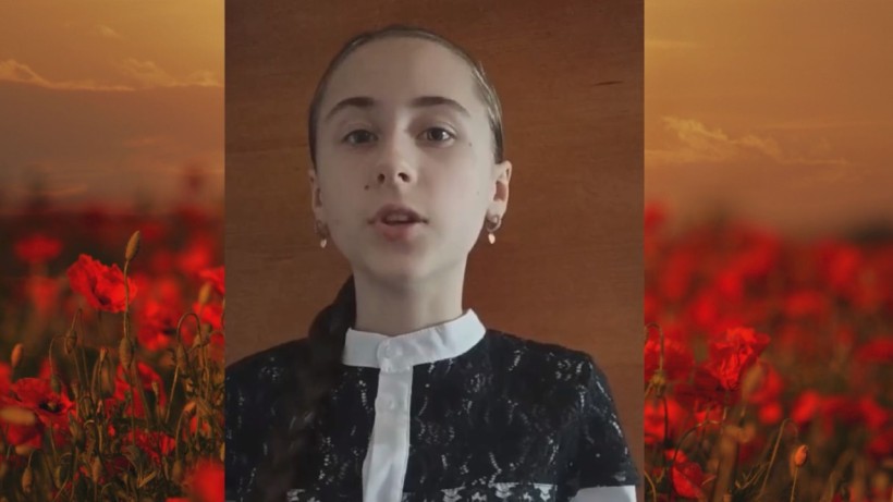 Учасниця фестивалю читає вірш на фоні зображення макового поля