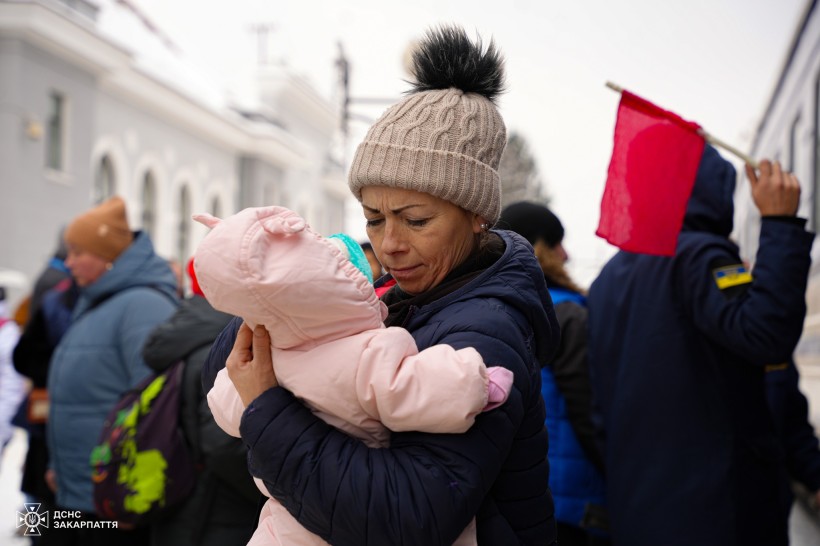 Жінка тримає на руках немовля на вокзалі поруч з евакуаційним потягом