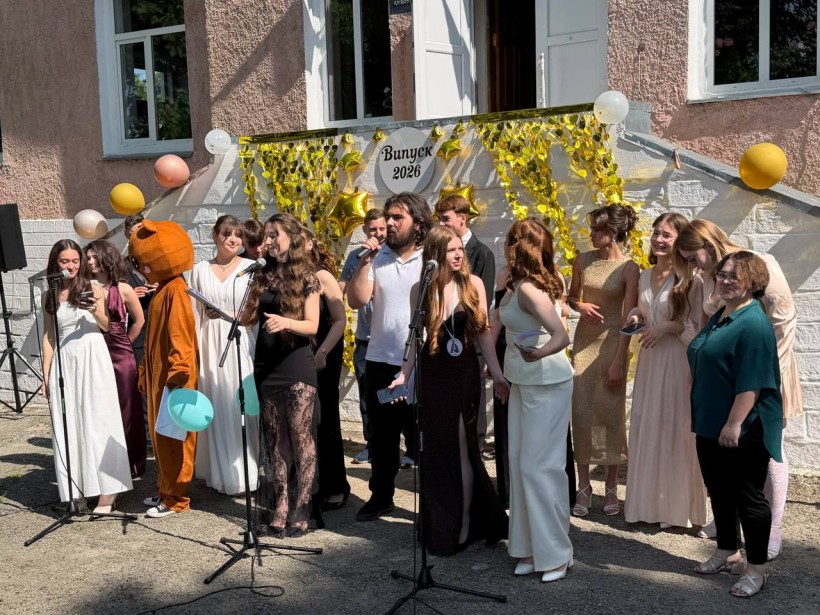 Випускники та викладачі виступають з мікрофонами на сходах святково прикрашеної будівлі