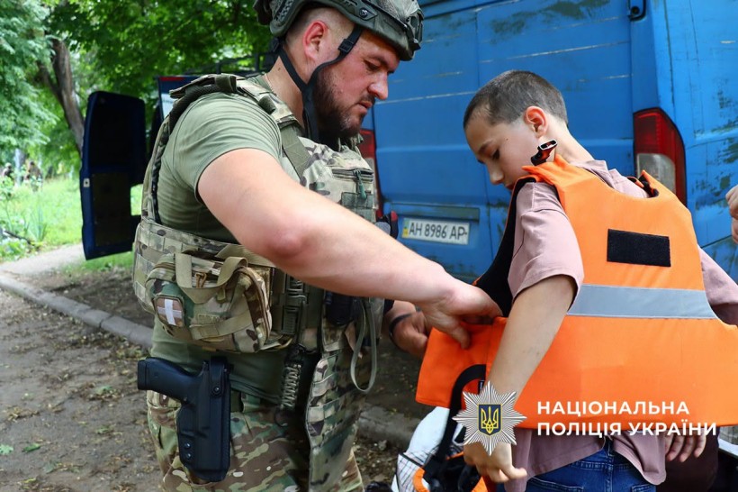 Поліцейський допомагає дитині вдягнути бронежилет та каску