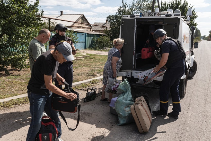 Рятувальники евакуаційної групи «ФЕНІКС», допомагають вантажити речі до автомобіля. Жінки та чоловік стоять з валізами.