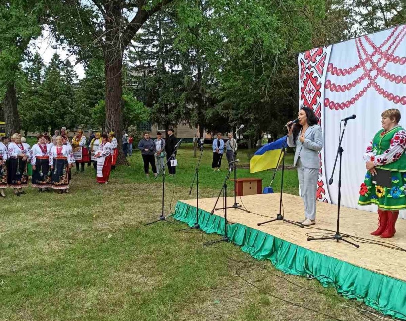 Представниця громади на сцені біля мікрофона. З боку майорить прапор України.
