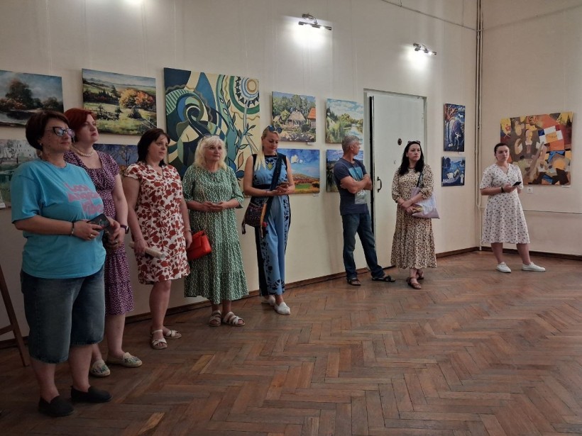 Група відвідувачів стоїть у виставковій залі та розглядає картини на стінах