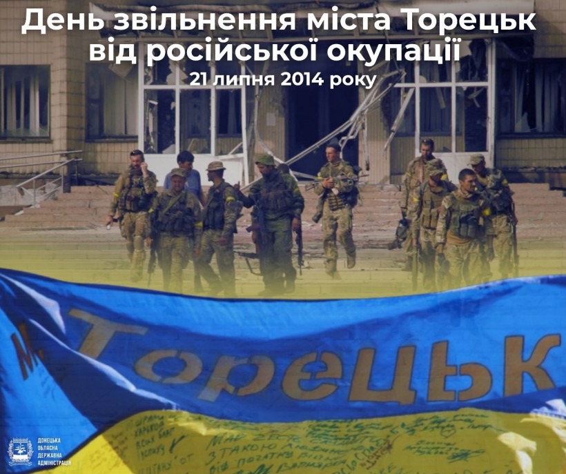 Українські солдати в камуфляжі стоять перед пошкодженою будівлею, тримаючи в руках зброю. На передньому плані — український прапор з написом. Атмосфера передає стійкість і звільнення. Напис зверху: «День звільнення міста Торецьк від російської окупації, 21 липня 2014 року».