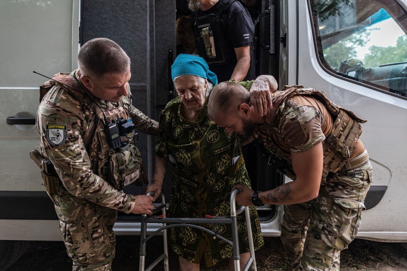 Співробітники поліції допомагають літній жінці, одного з поліцейських жінка обіймає рукою за шию, іншою рукою тримає ходунки.