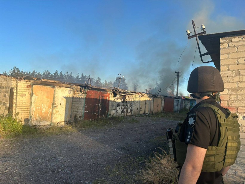 Правоохоронець дивиться на гаражі, кі палають після обстрілу.