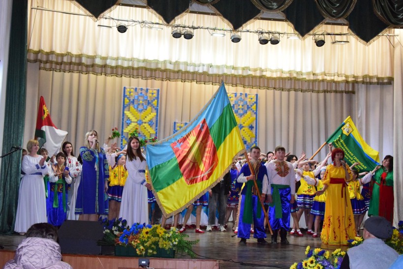 На сцені народний колектив у вишиванках, чоловіки тримають прапор громади.