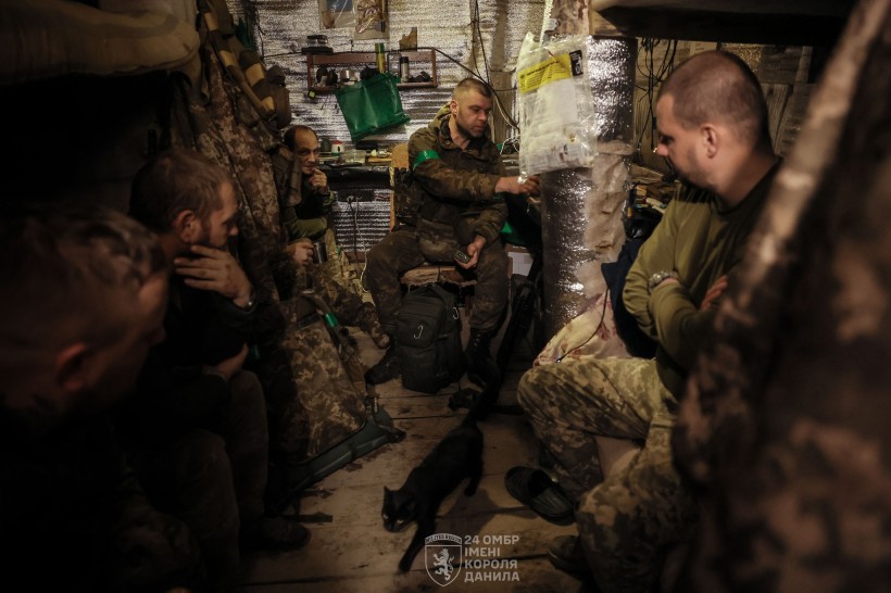 Група піхотинців сидить у бліндажі. Один з них щось розповідає, інші уважно слухають.