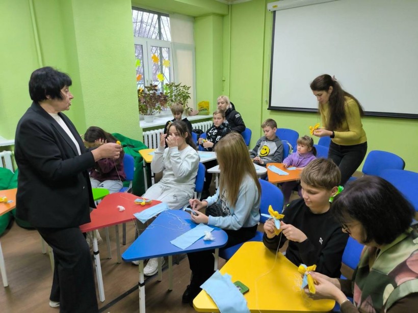 Діти, учасники заходу, в м. Дніпро виготовляють мотанки-обереги з жовтої та блакитної тканини для захисників та захисниць
