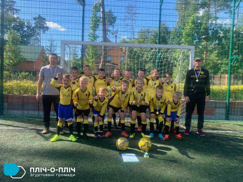 Юні футболісти стоять біля футбольних воріт, по обидва боки тренери, попереду - футбольні м'ячі.