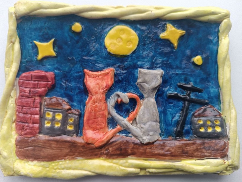 Яскравий барельєф з солоного тіста: рудий і сірий коти сидять на даху під нічним небом із місяцем і зірками, хвости яких утворюють серце