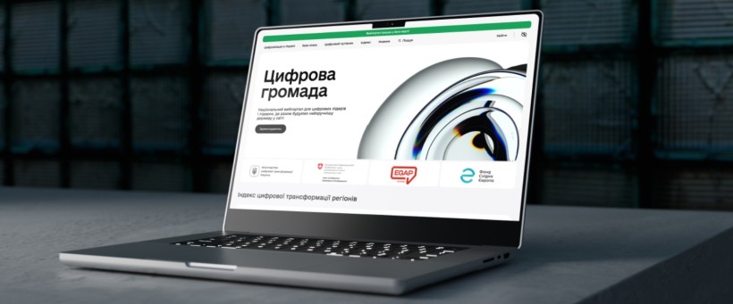 На темній поверхні лежить стильний ноутбук, на екрані якого відображається веб-сайт під назвою «Цифрова громада» з сучасною графікою та логотипами, що передають інноваційність.