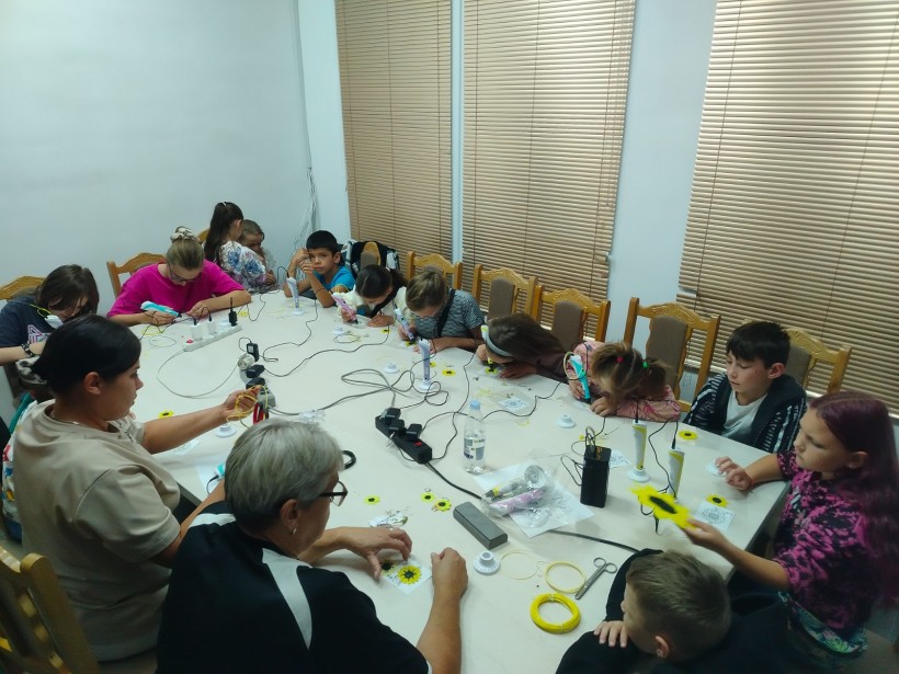 Діти та дорослі за великим столом створюють об'ємні соняшники за допомогою 3D-ручок