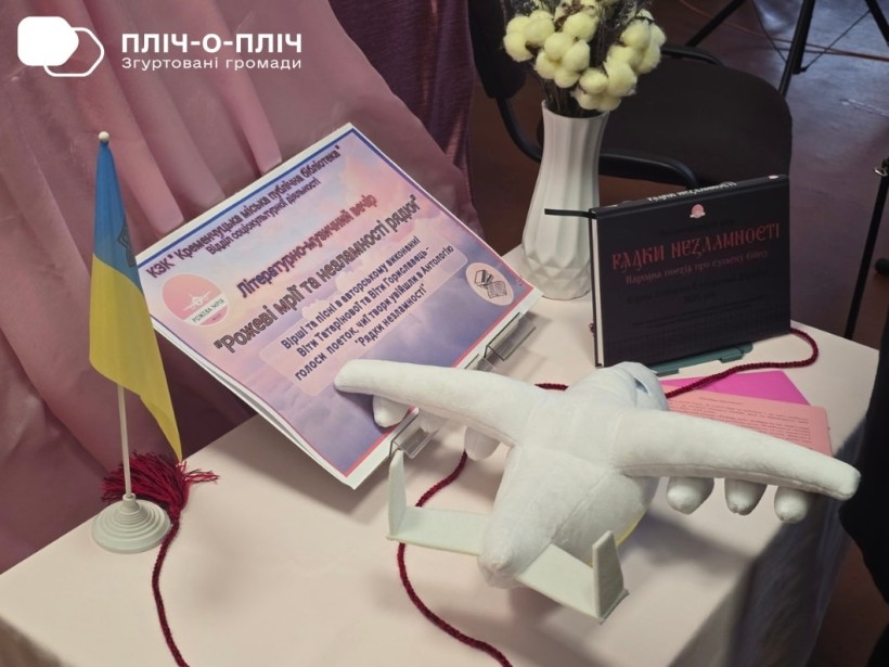 На столі лежать афіша заходу,квіти, м'який літачок та стоїть прапор України.