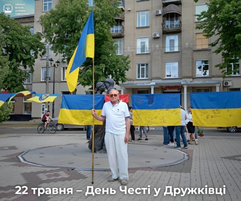 На площі в Дружківці, 22 травня, люди святкують День Честі. Чоловік з прапором стоїть поруч з державним прапором України та символікою