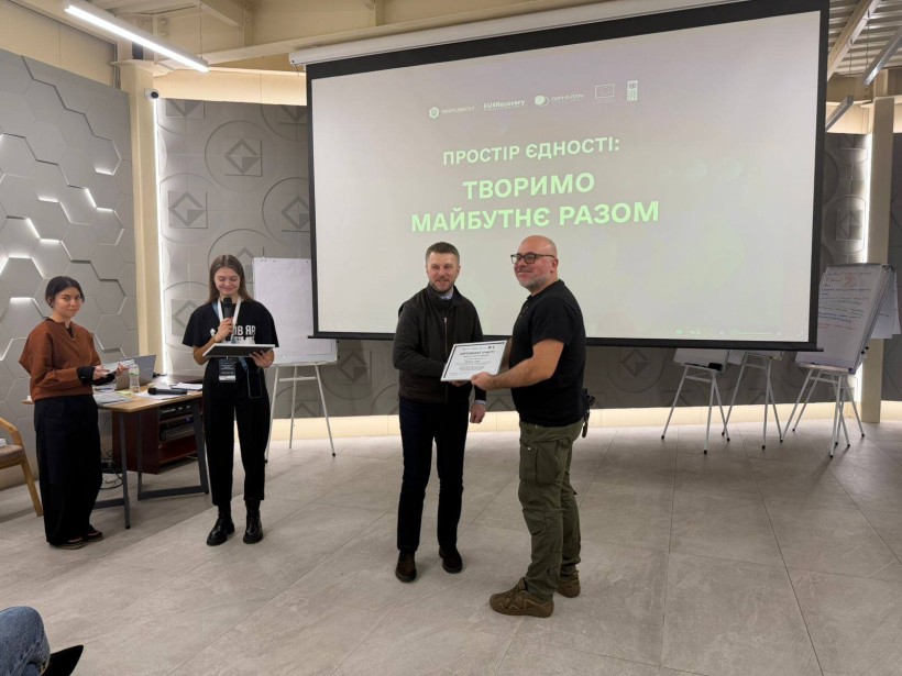 Начальник міської військової адміністрації Сергій Чаус тримає сертифікат учасника форуму, поруч стоїть представник громади