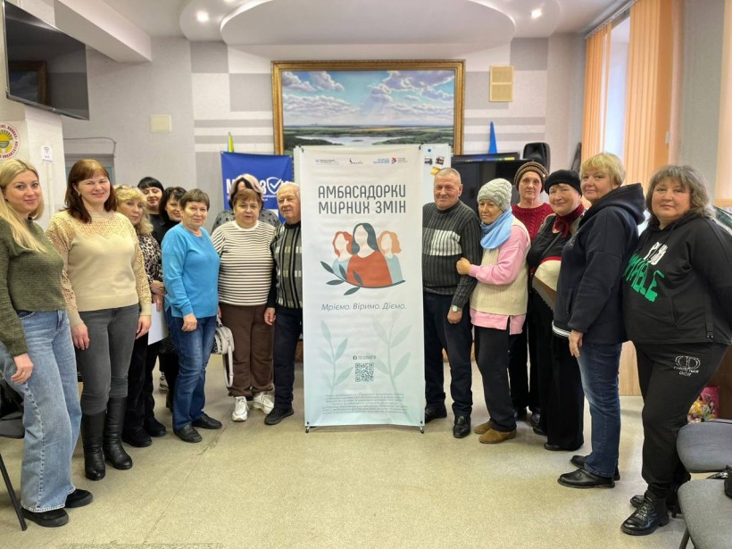 Спільне фото учасників діалогової зустрічі, посередині борд організаторів.