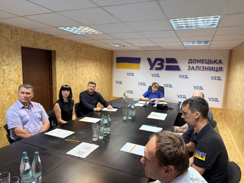Представники регіональної філії "Донецька залізниця" АТ "Укрзалізниця" сидять за великим столом у конференц-залі і є учасниками онлайн сесії в межах ярмарку вакансій. На задньому плані розміщений банер з логотипом "Укрзалізниця" та написом "Донецька залізниця".