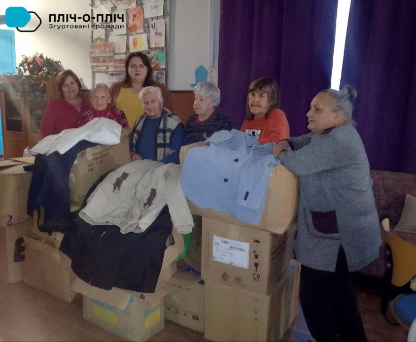Людям похилого віку та з інвалідністю надана гуманітарна допомога у вигляді осінньо-зимового одягу. Чоловіки та жінки стоять біля ящиків з одягом.