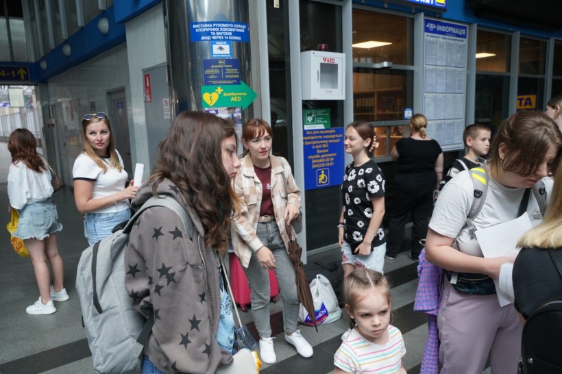 Група дівчат, спілкуються в будівлі залізничного вокзалу. Позаду них каси продажу квитків.