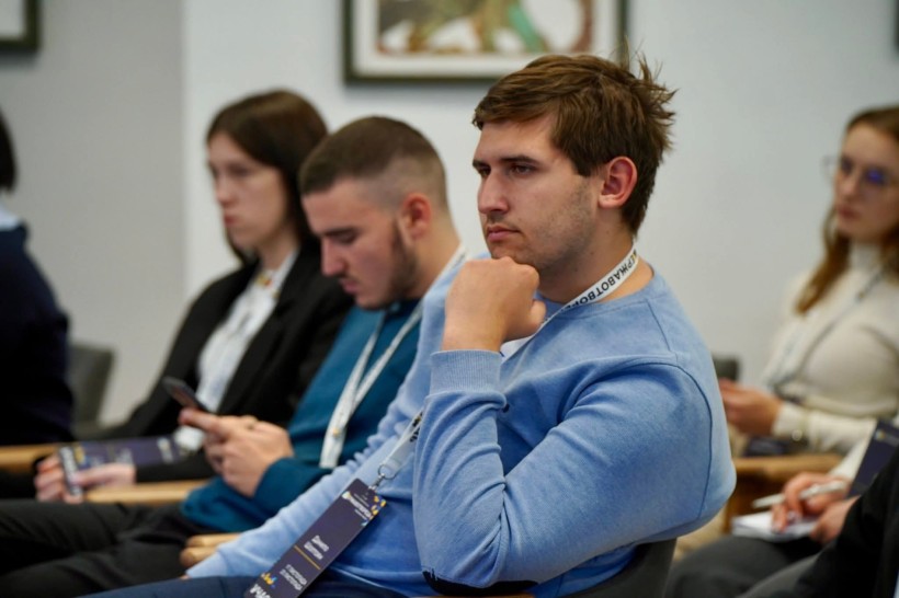 Учасники заходу. Молодий чоловік тримає руку біля обличчя та слухає.