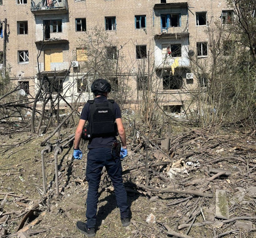 Правоохоронець стоїть біля зруйнованого окупантами багатоповерхового будинку