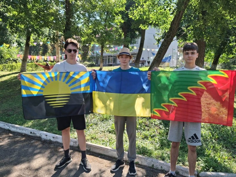 троє хлопців та території табору тримають прапори
