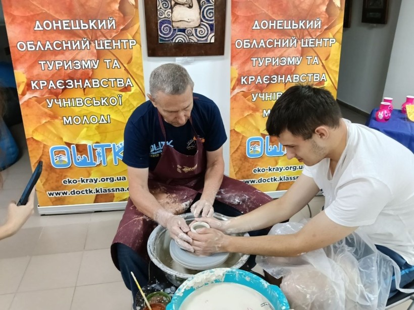 Учасник майстер-класу під керівництвом майстра формує глиняний виріб на гончарному колі.