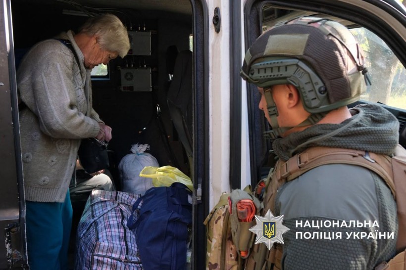 Жінка вантажить речі до евакомобіля, поруч стоїт полійцейський