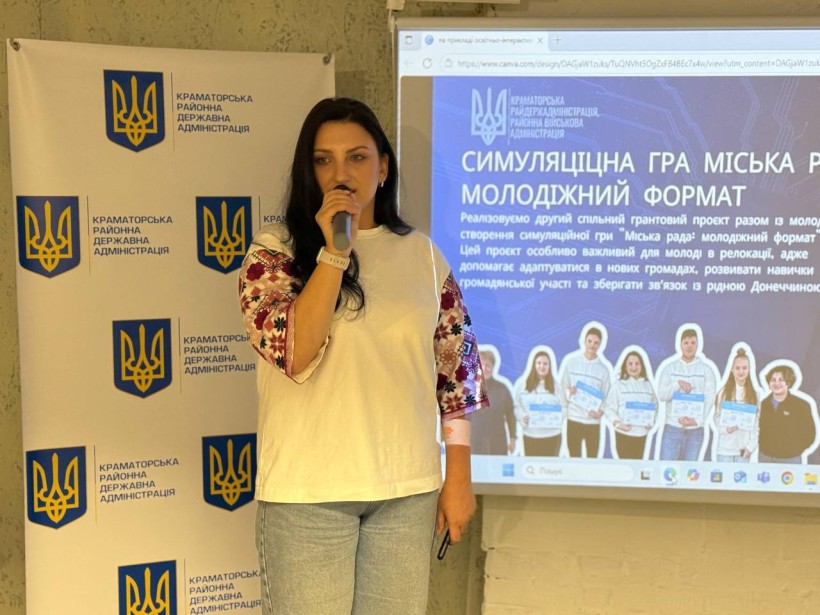 Учасниця заходу говорить у мікрофон. На задньому плані слайди презентації від молодіжної ради.