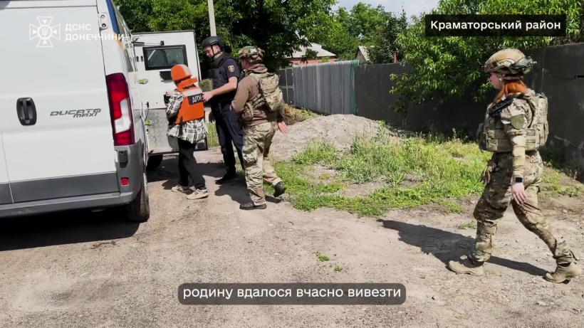 Евакуація мирного населення. Рятувальники у засобах захисту супроводжують дитину у помаранчевому бронежилеті до автобуса.