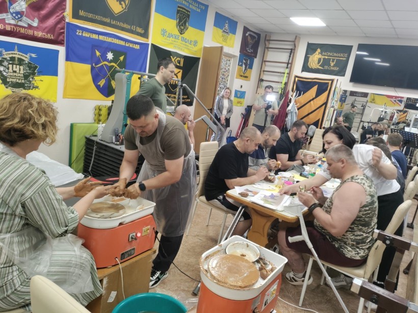 Загальний план приміщення для реабілітації, де військові займаються гончарством та розписом керамічних фігурок за великим столом