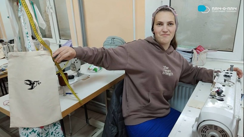 Студентка за швейною машинкою тримає екоторбу з вишивкою